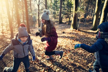 Drie kinderen lopend al lachend achter elkaar in het bos