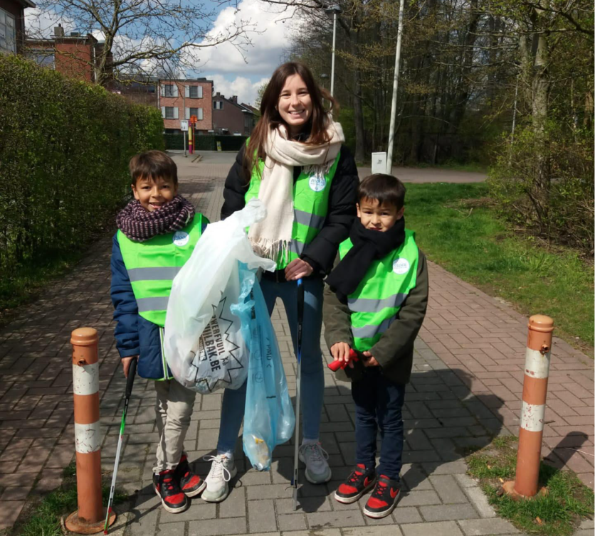 Twee jongens en een vrouw met vuilzakken vast, lachen samen tijdens het plandelen.