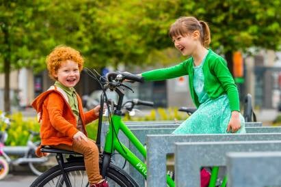 Een meisje fietst met een jongen vooraan op haar bagagedrager