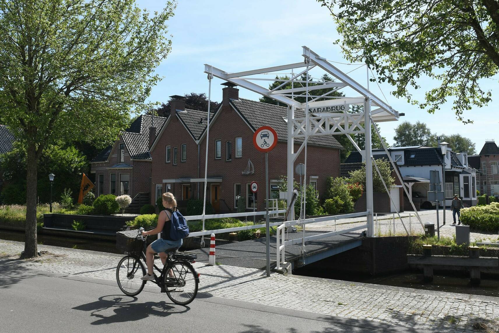 Foto van een dame die langs een oude brug fietst