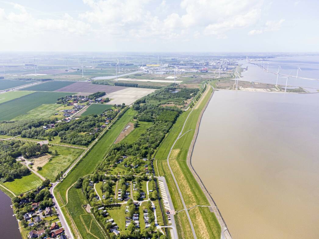 Luchtfoto van landelijk beeld langs het water met op de achtergrond windmolens