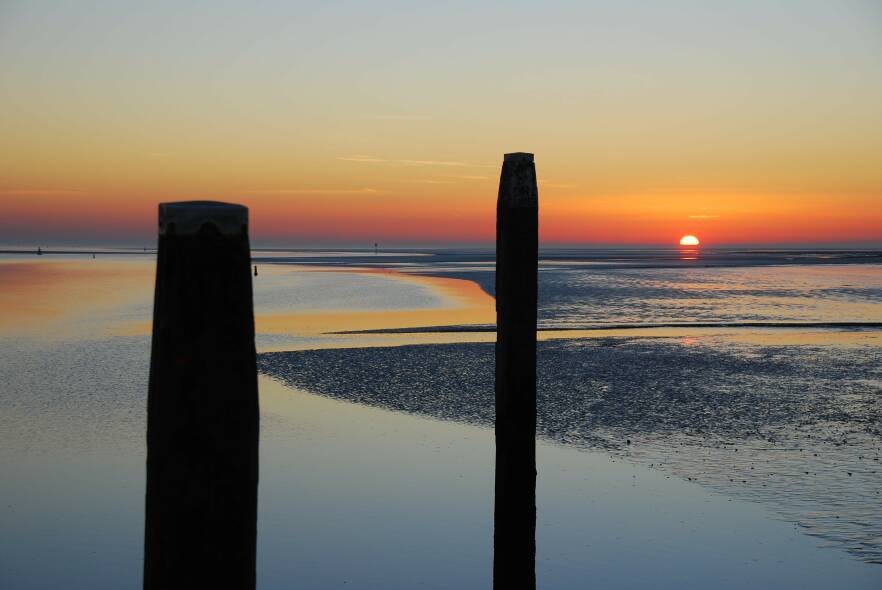 Beeld van twee palen in de zee bij eb tijdens een zon die in de zee zakt