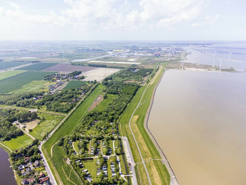 Luchtfoto van landelijk beeld langs het water met op de achtergrond windmolens