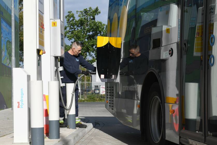 Beeld van een bus waar een man waterstof tankt