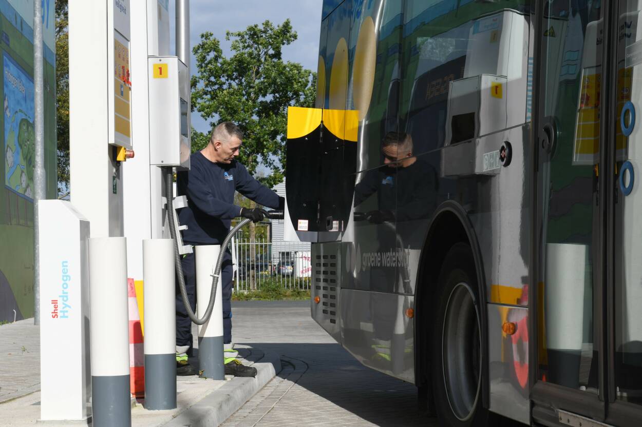 Beeld van een bus waar een man waterstof tankt