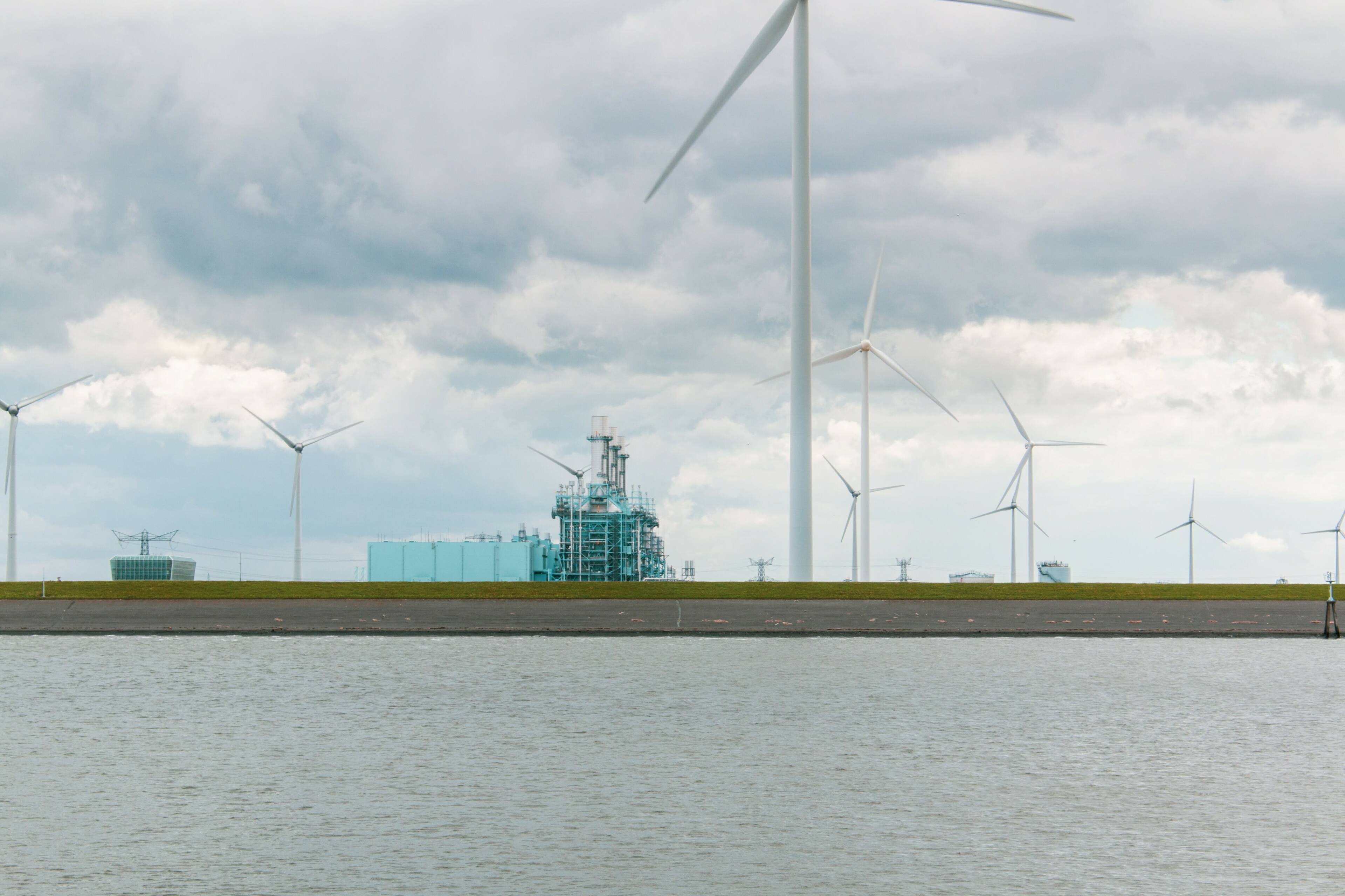 Beeld ver verschillende windmolens langs het water in industrieel gebied