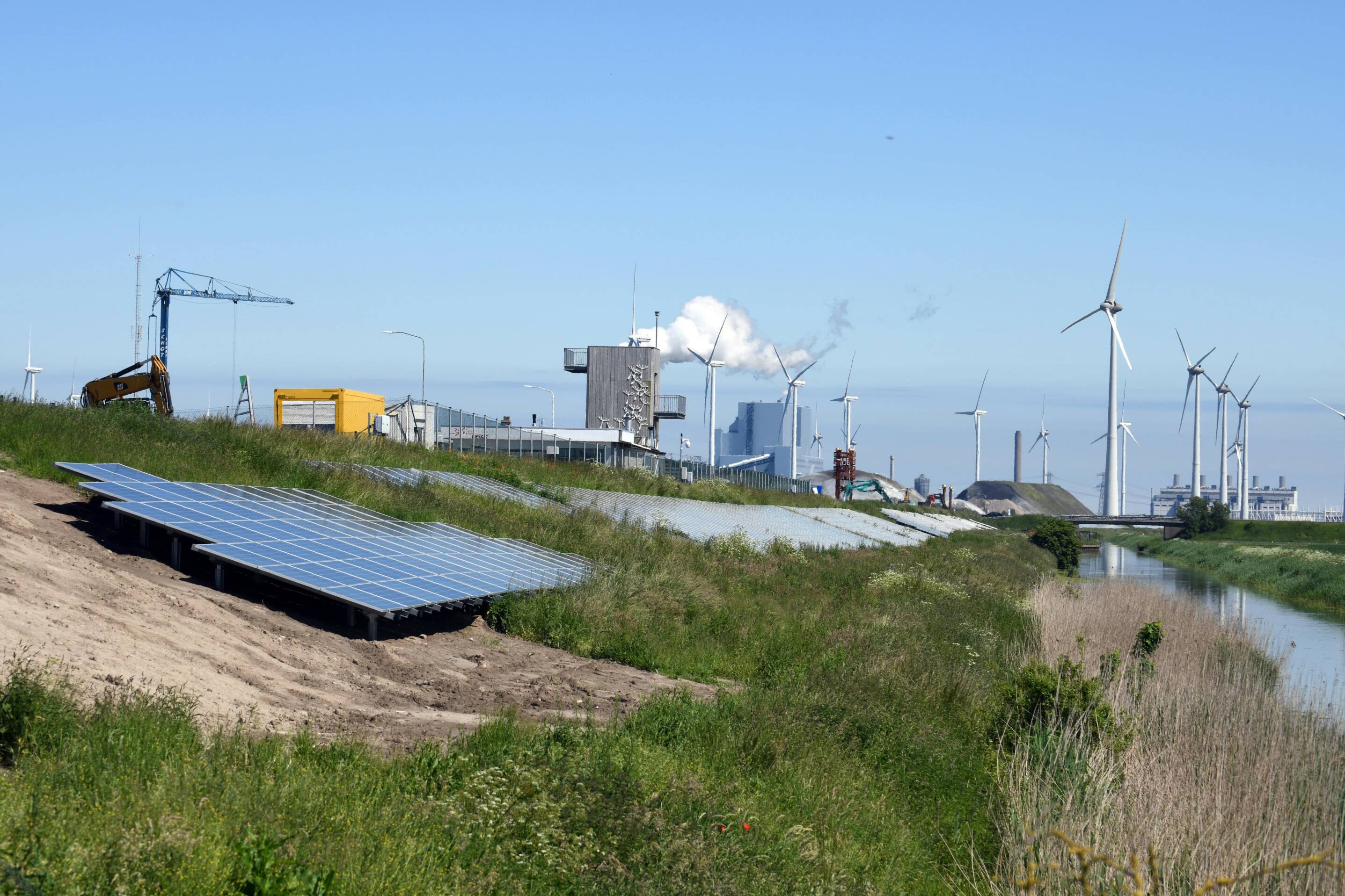 Beeld van zonnepanelen op de grond in het gras binnen industrieel gebied