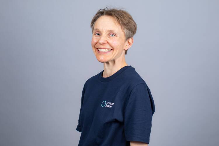 A headshot photo of Jenny Cane - the background is grey with Jenny stood in the centre with a big smile