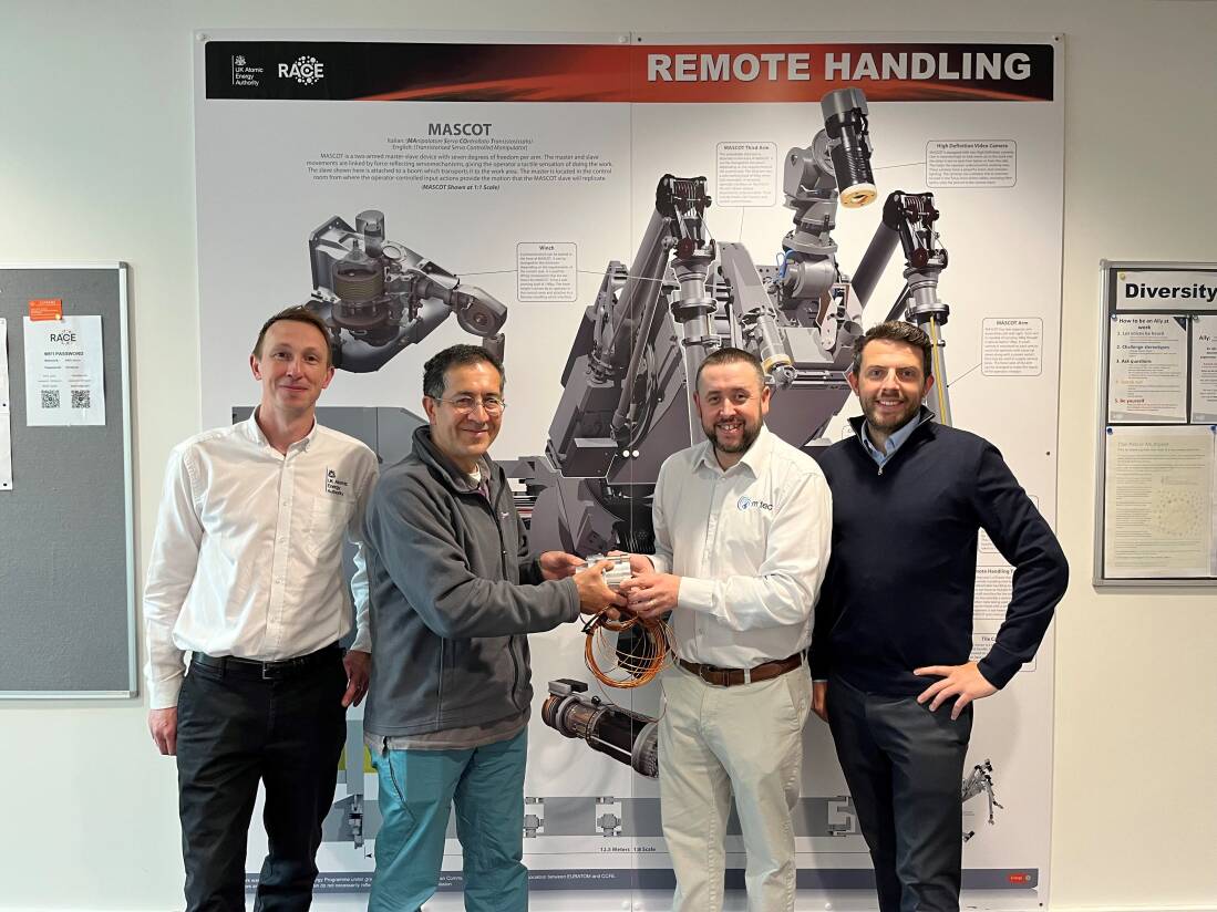 Four men stood with their backs to a wall, two men in the middle are holding a scientific device