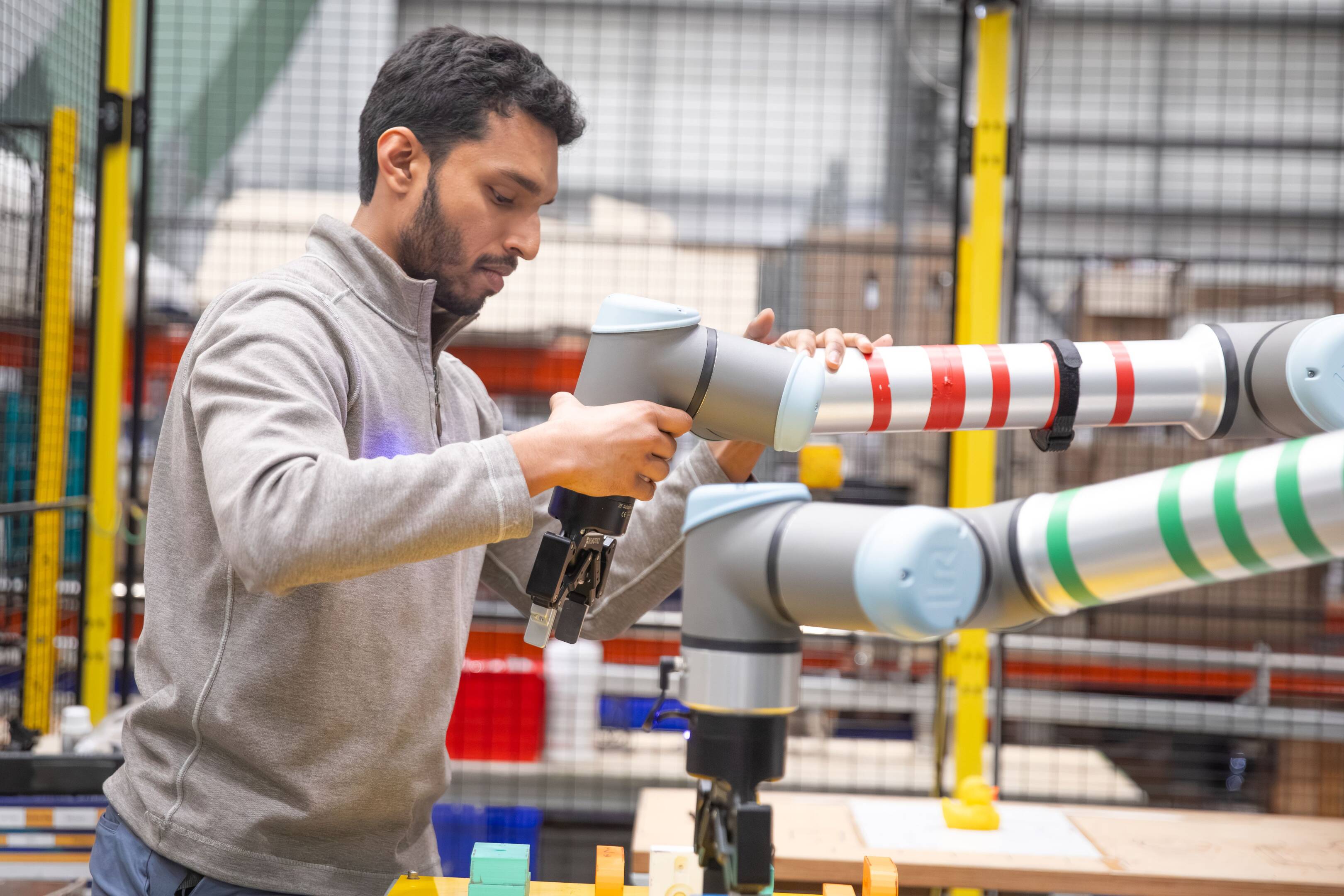 A person in a workshop at UKAEA's Culham campus adjusting and positioning a robotic arm. The workspace includes safety fencing and small objects on the work surface