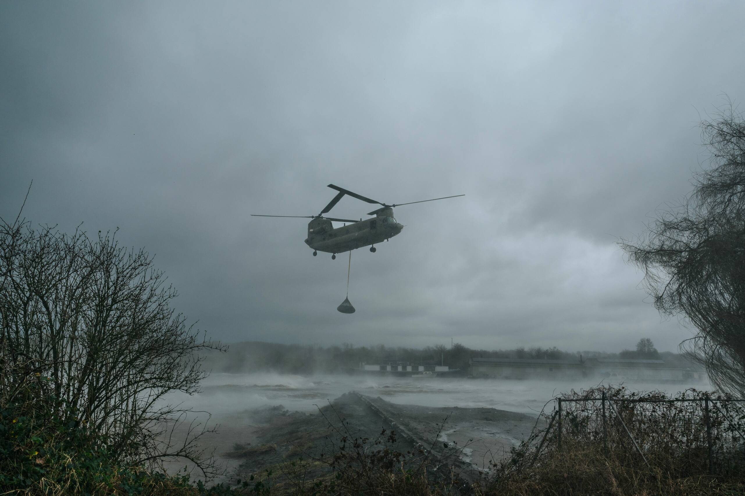 Foto van een Chinook helikopter van Defensie die rockbags in een gat plaatst in de overlaatdam bij Roermond.