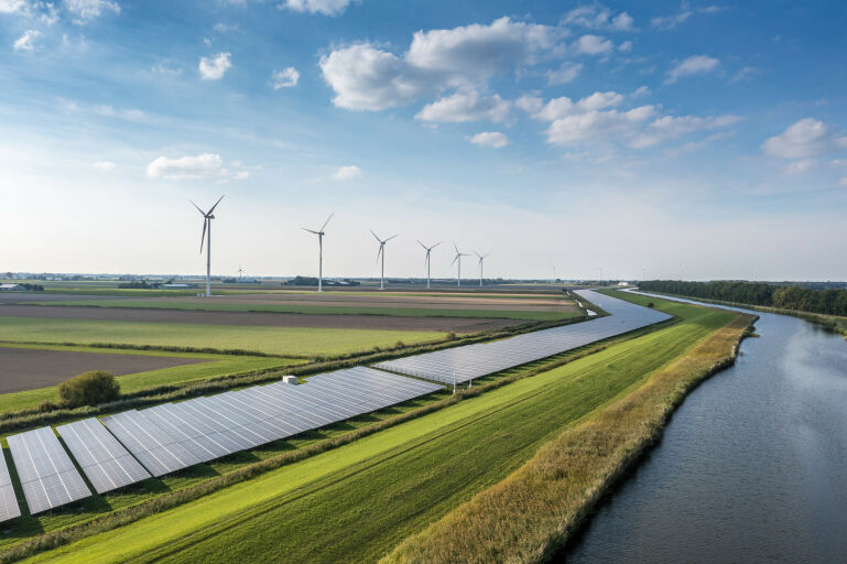 Foto van een Nederlands landschap met op de voorgrond een rivier en een lange rij zonnepanelen en in de verte windmolens