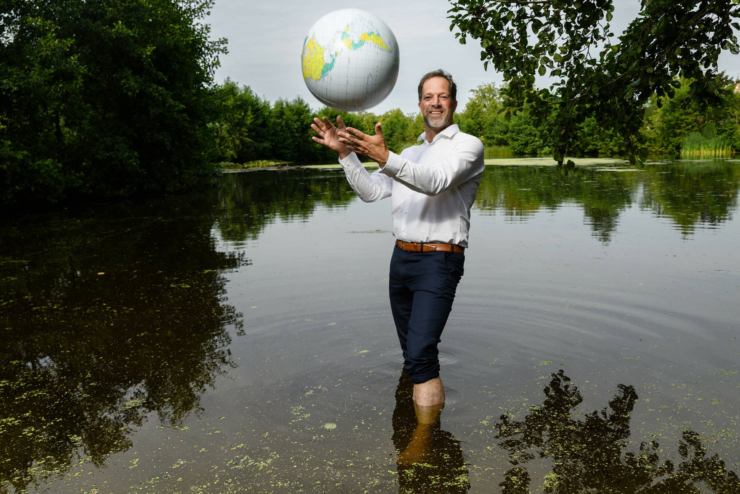 Foto van Mark van der Werd, de nieuwe directeur van STOWA, met een opblaasbare wereldbol in zijn handen terwijl hij met blauwe broek en wit overhemd in een meertje staat.