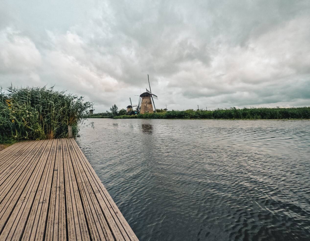 Foto van een Nederlands waterlandschap met op de voorgrond een steiger langs een sloot en op de achtergrond twee molens