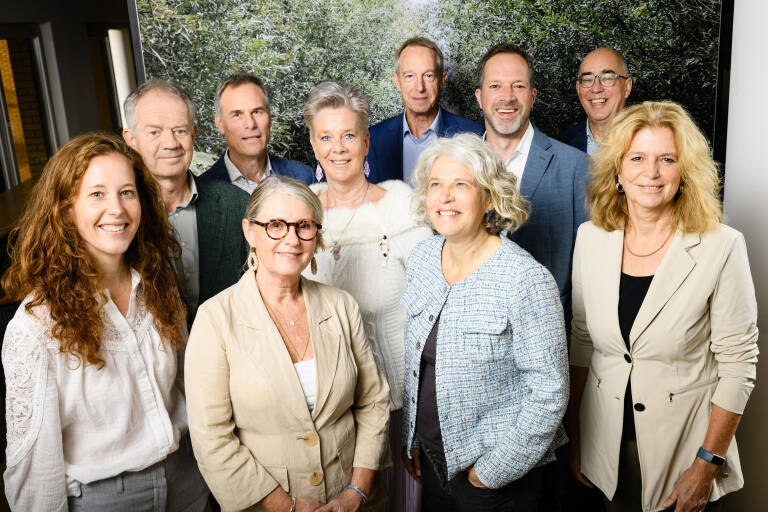 Foto van een Nederlands landschap met op de voorgrond een rivier en een lange rij zonnepanelen en in de verte windmolens
