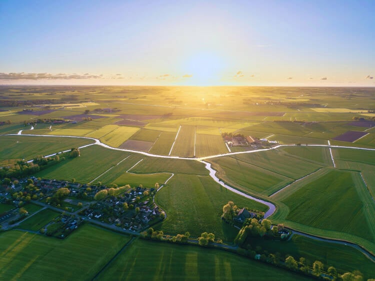 Foto van een Nederlands landschap met op de voorgrond een rivier en een lange rij zonnepanelen en in de verte windmolens