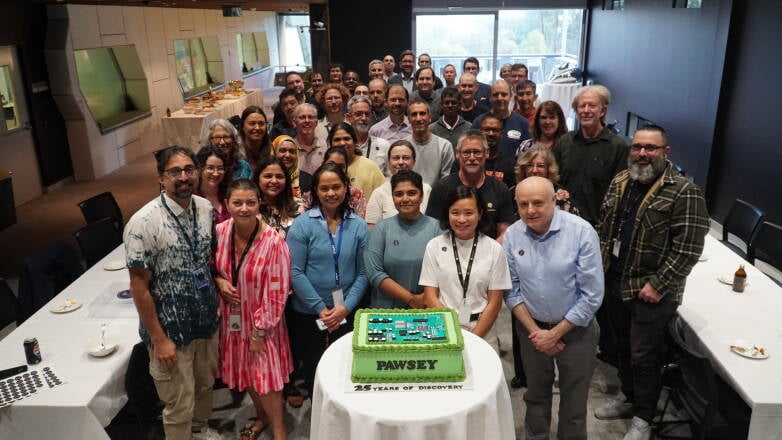 Whole team photo of Pawsey staff surrounding a cake for Pawsey's 25 years of discovery
