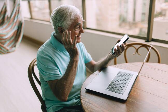Foto van een oudere man die met zijn telefoon aan het videobellen is