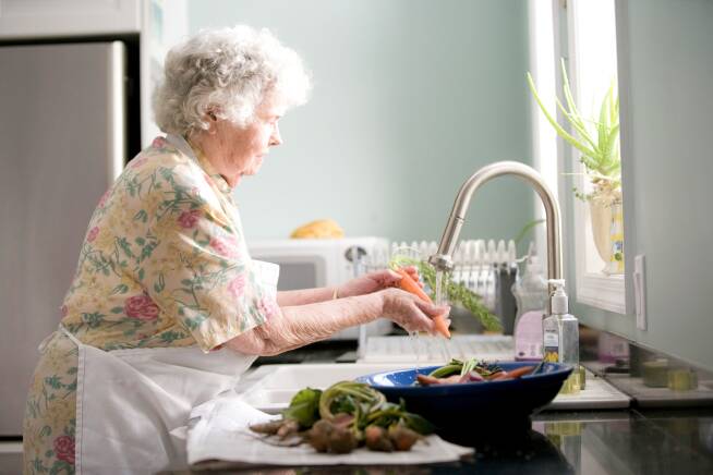Foto van een oudere vrouw die groenten aan het wassen is in de keuken.