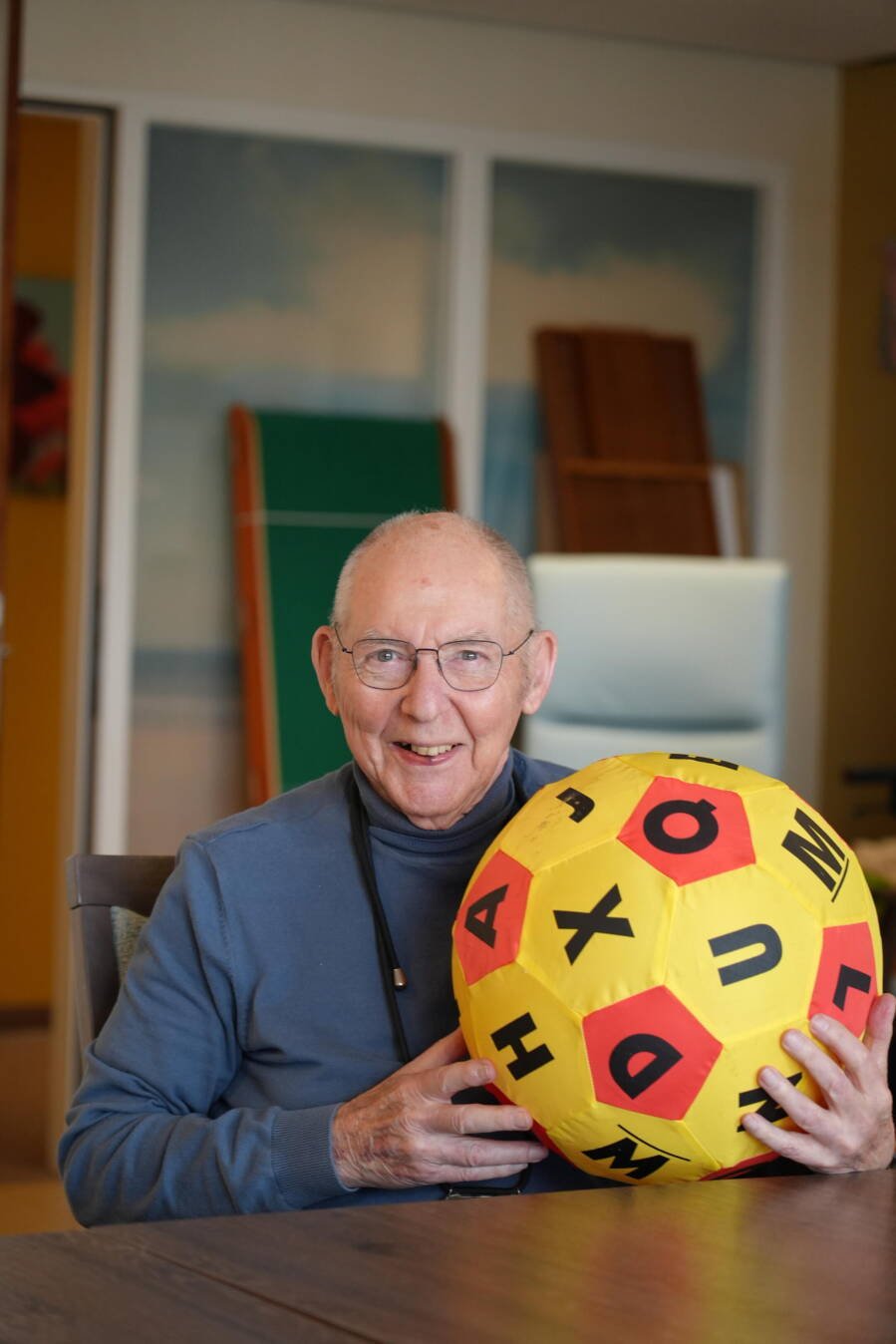 Foto van een oudere meneer met een grote opgeblazen bal waar allemaal letters op staan.