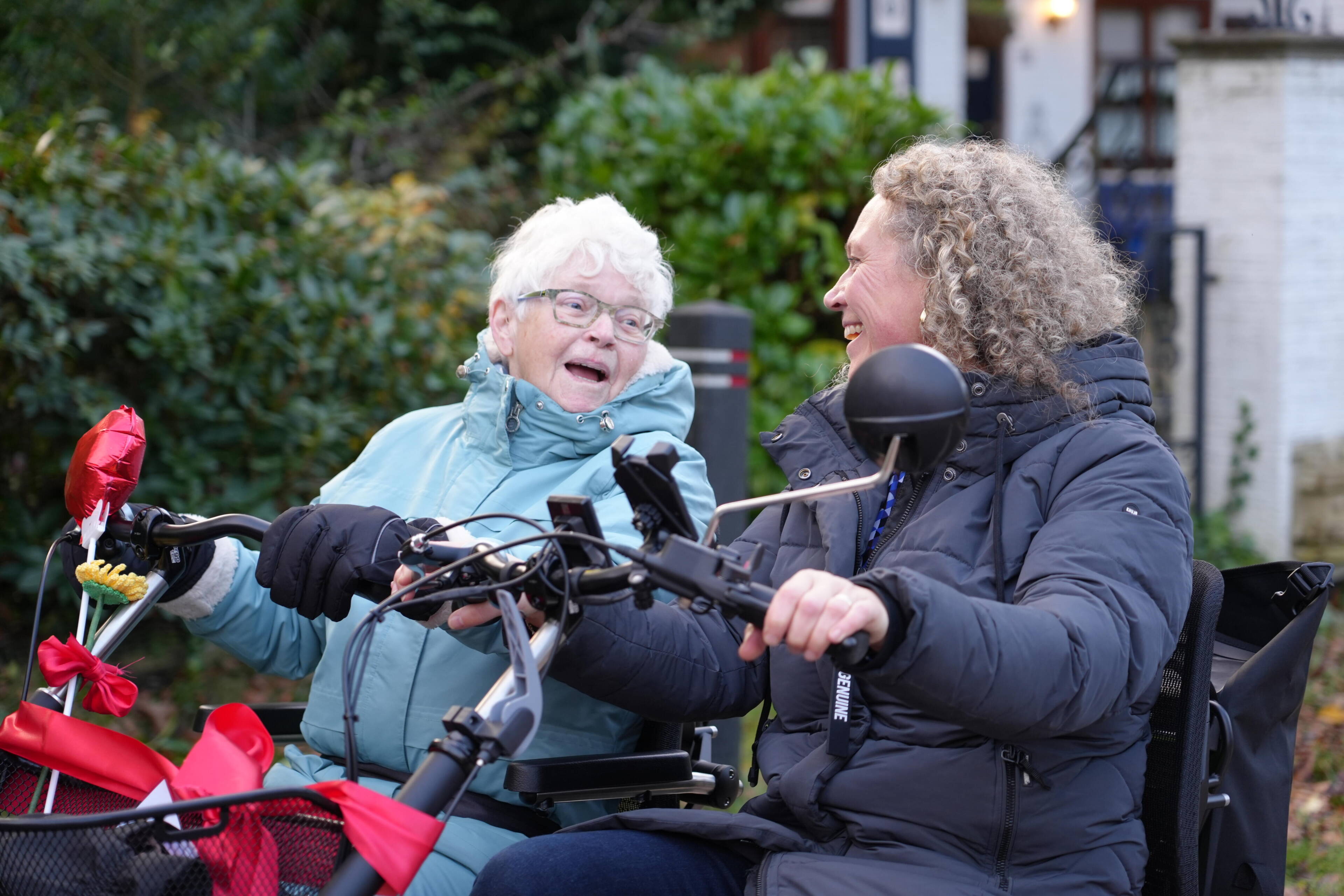 Een oudere vrouw die naast een zorgmedewerker fietst. Ze lachen naar elkaar.