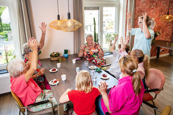 Foto van een oudere mevrouw die lachend met haar armen omhoog beweegt.