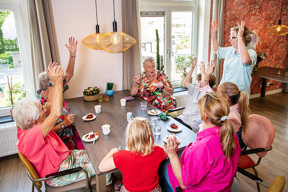 Foto van een oudere mevrouw die lachend met haar armen omhoog beweegt.