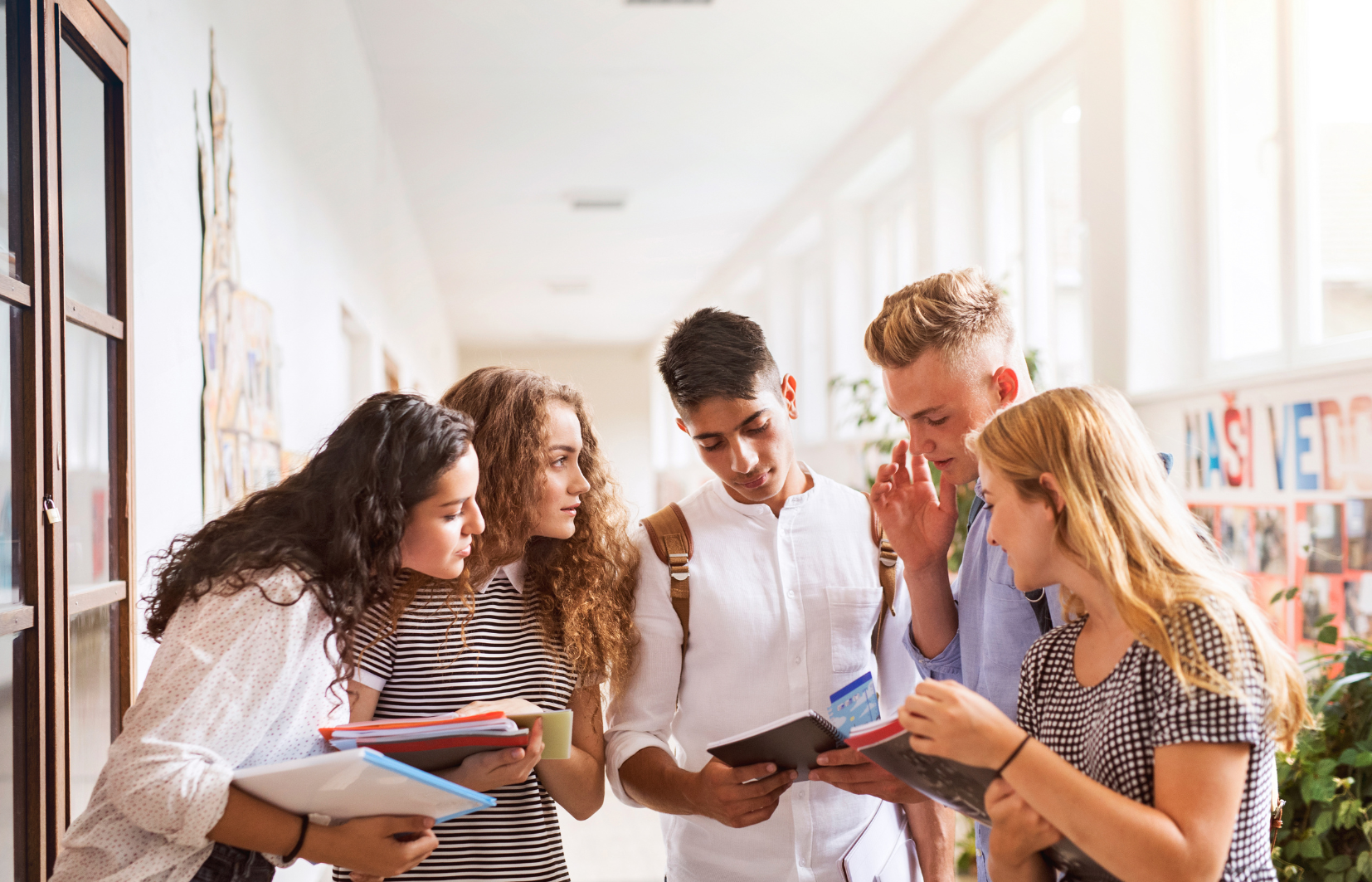 vijf jongeren met elkaar in gesprek in de hal van een schoolgebouw