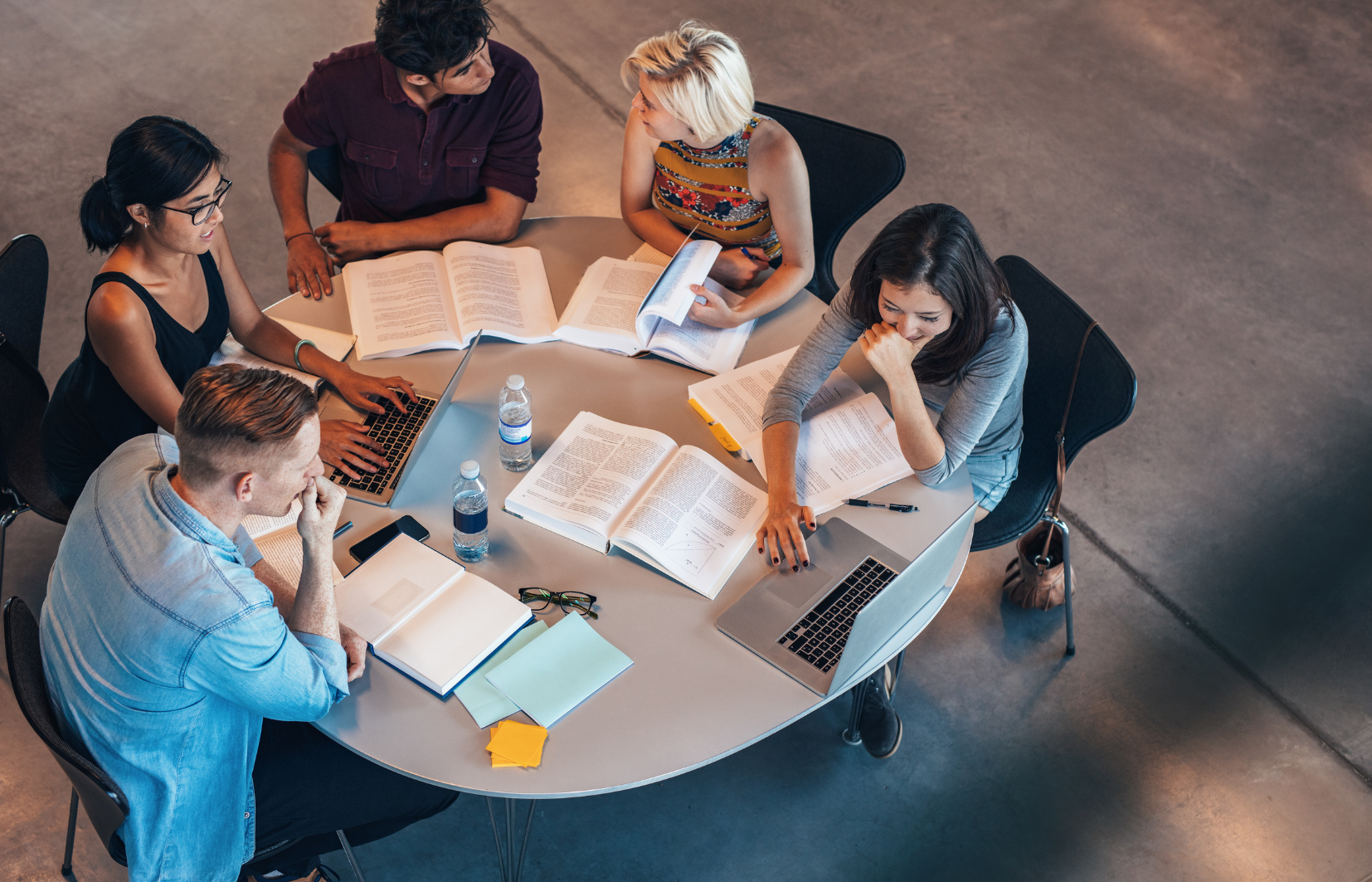 personen aan een ronde tafel in overleg, van bovenaf bezien. op tafel liggen boeken.