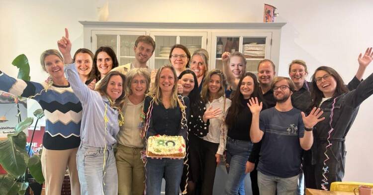 Groepsfoto van het ECIO-team, met leden die glimlachen naar de camera; enkele personen steken de rechterarm met duim omhoog op.