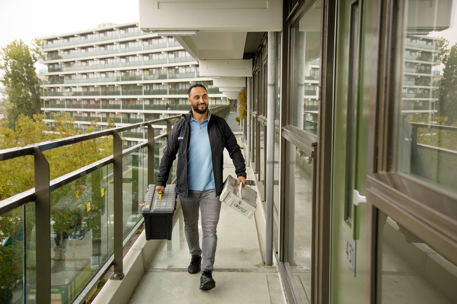 We zien een reparatiemedewerker over een portiek lopen, onderweg naar een huurder