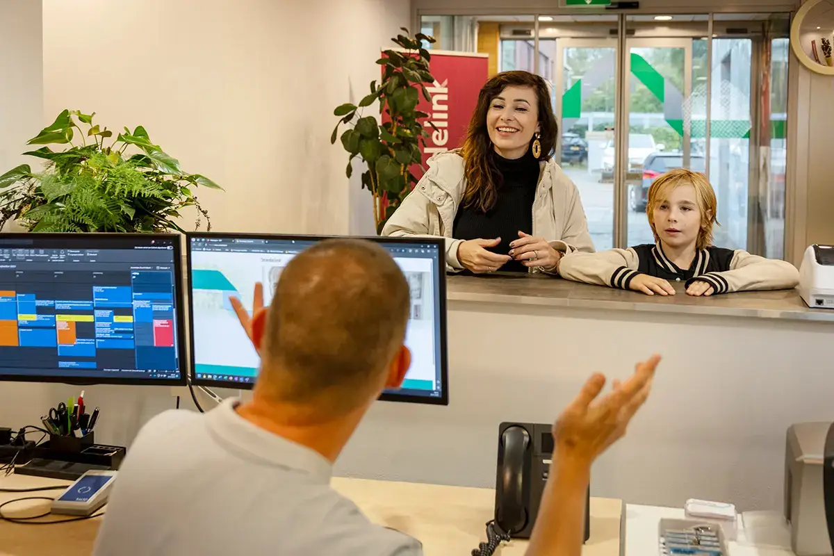 Een moeder en kind worden welkom geheten bij een balie op locatie bij Stedelink