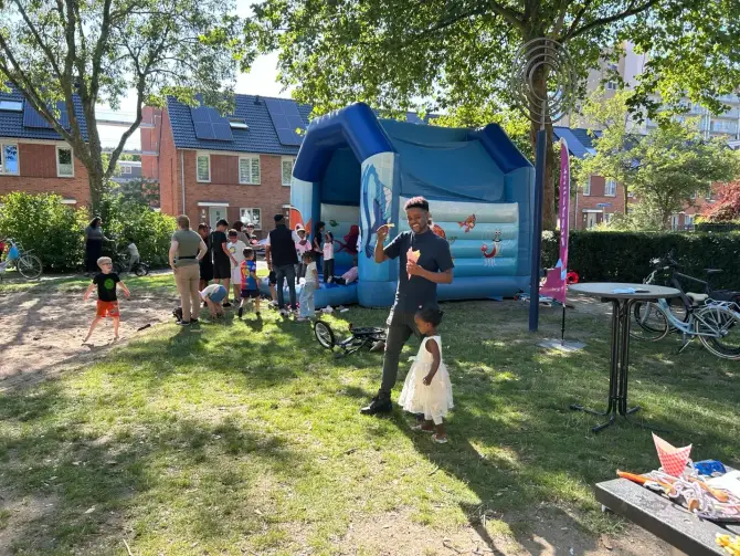 Bewoners en kinderen genieten van buurtfeest met springkussen in de speeltuin.