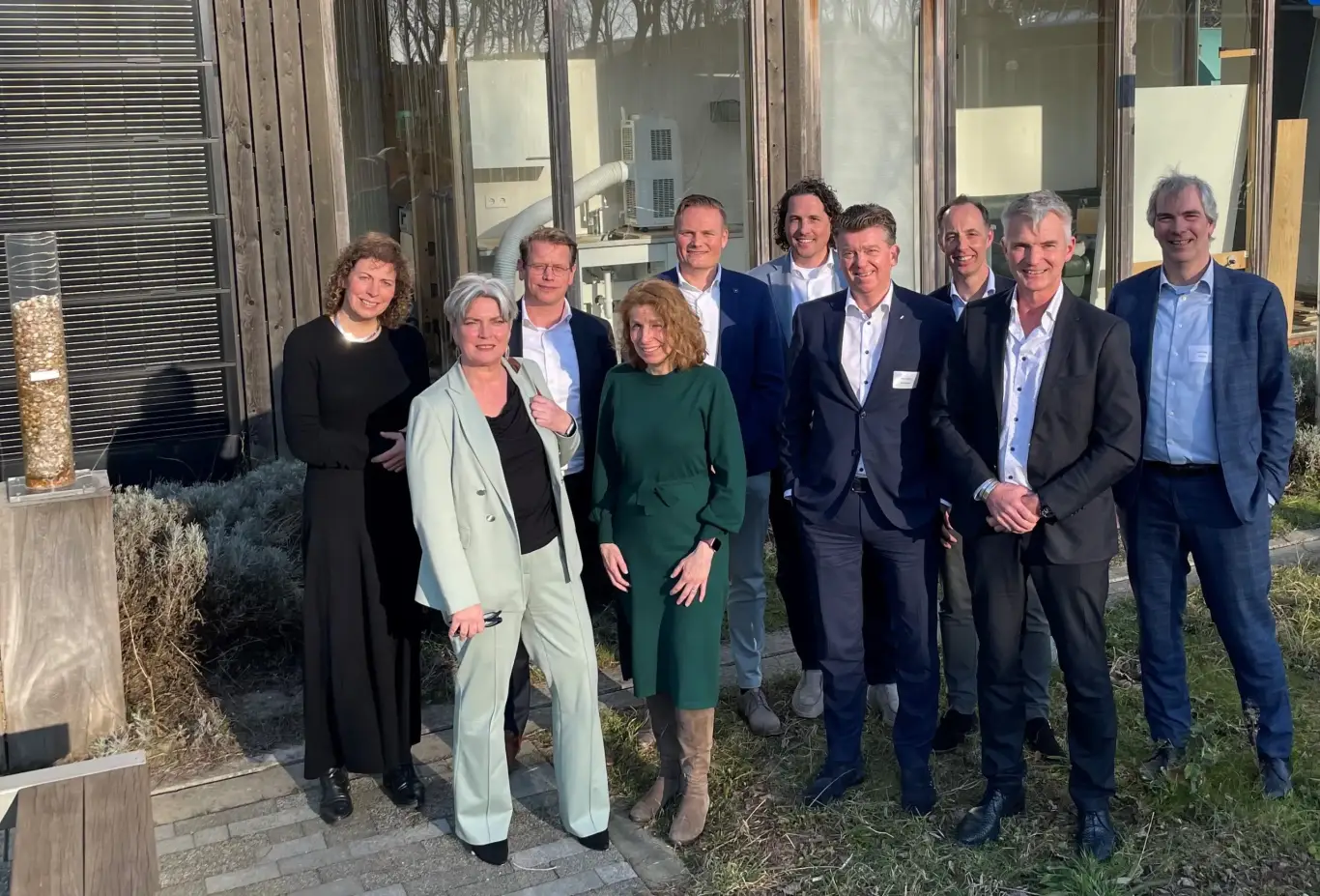 Groep samenwerkingspartners staat buiten bij gebouw en markeert eerste jaar samenwerking in renovatieproject.