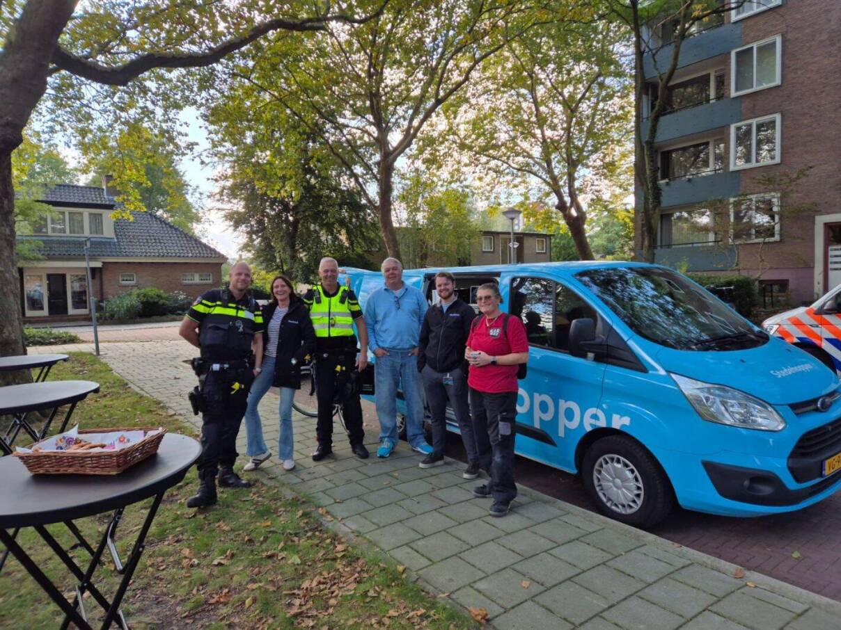 Groep samenwerkingspartners staat bij bus in woonwijk en werkt samen aan leefbare omgeving.