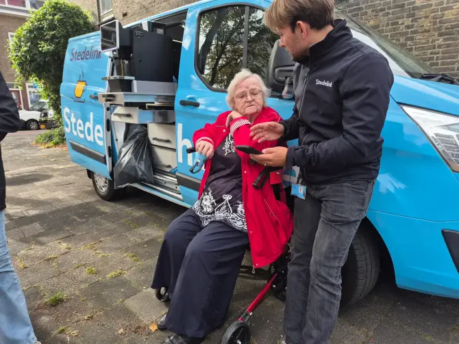 Medewerker in gesprek met bewoner bij mobiele ontmoetingsbus in de wijk.