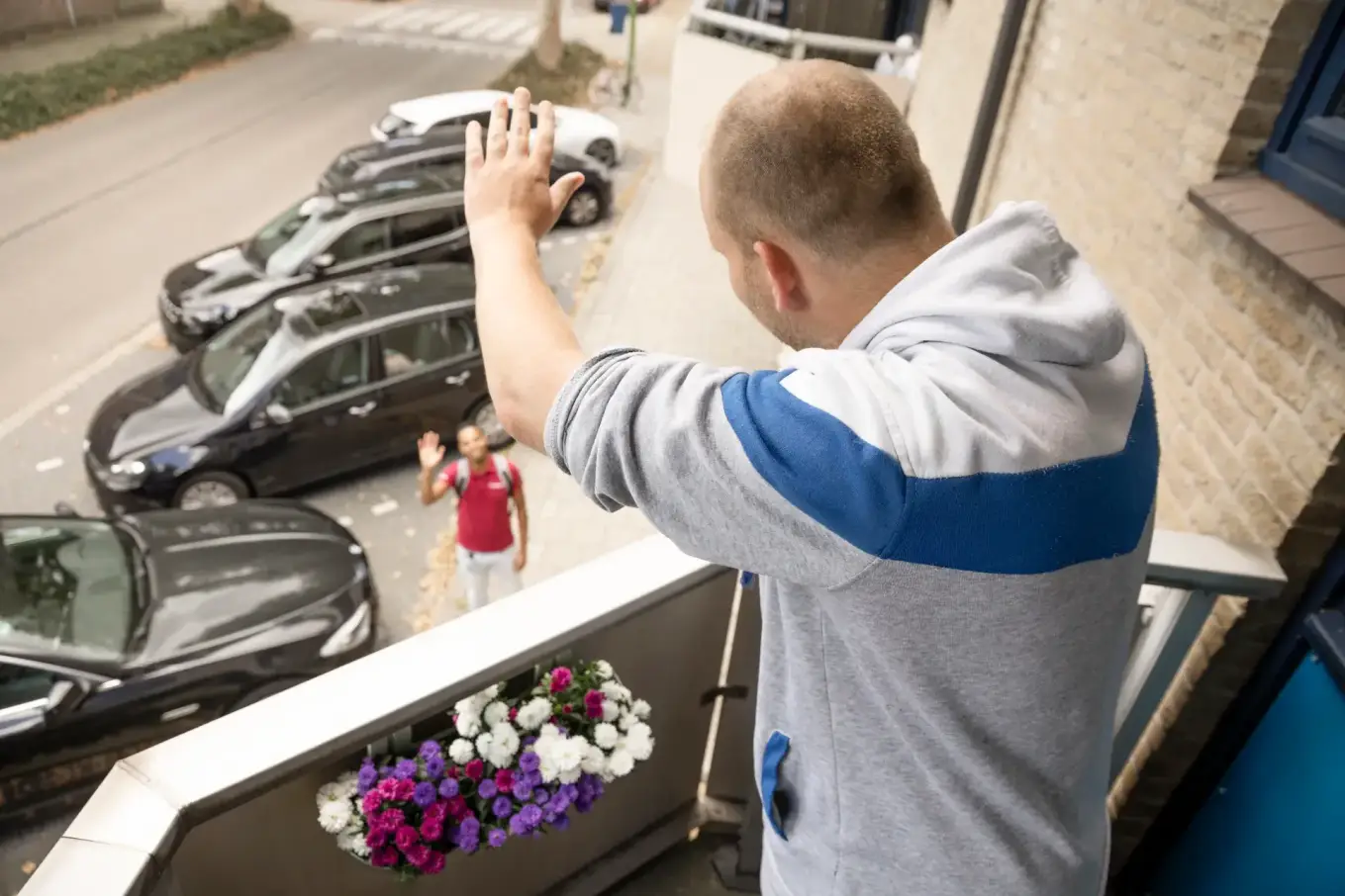 Bewoner op balkon zwaait naar een medewerker van Stedelink op straat.