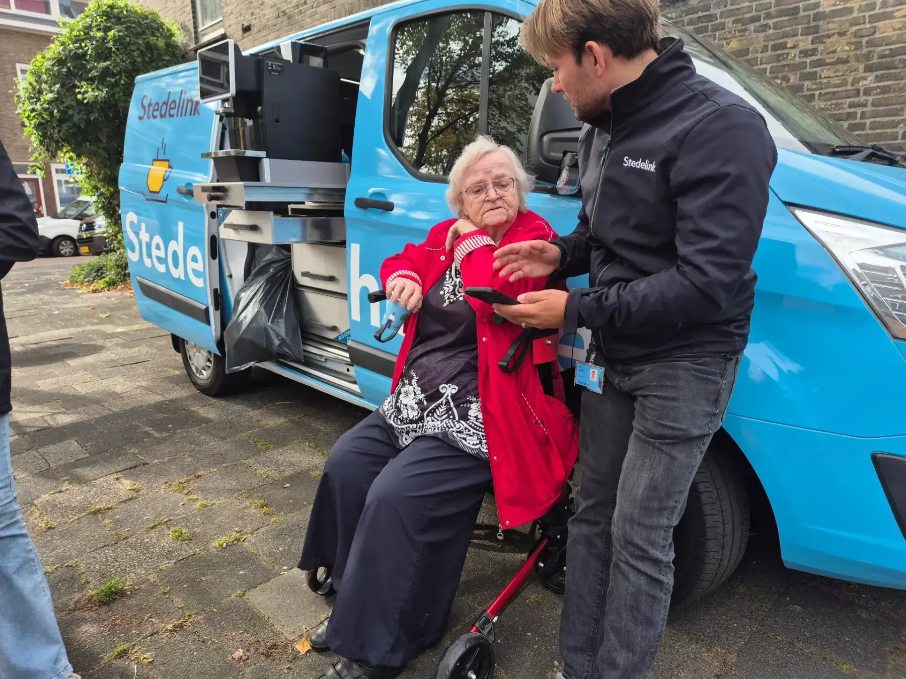 Medewerker in gesprek met bewoner bij mobiele ontmoetingsbus in de wijk.