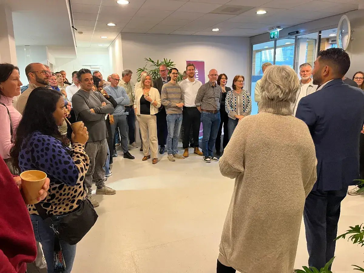 Collega&rsquo;s staan samen in kantoorruimte en luisteren naar presentatie tijdens bijeenkomst over organisatieverandering.