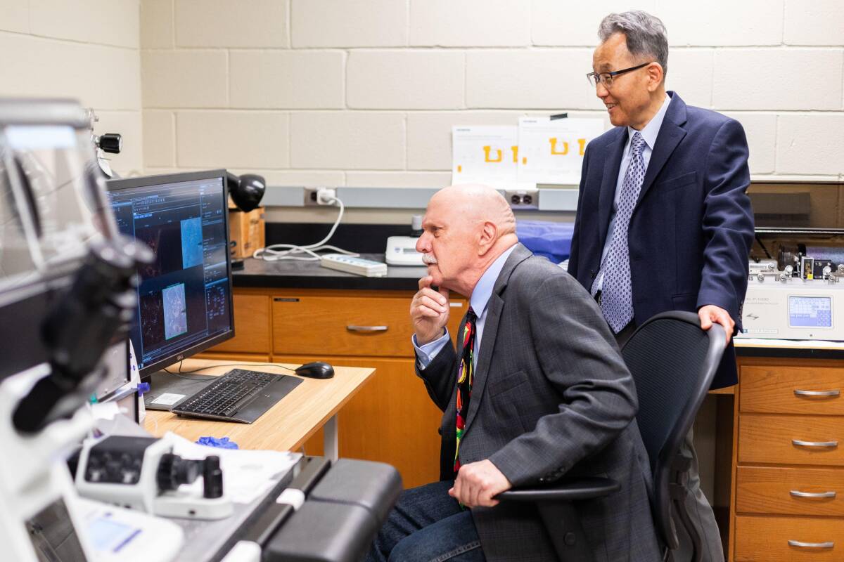 Dr. Wonhwa Cho stands next to Dr. Herb Paaren, who is looking at a monitor on a seat.