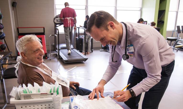 Medical professional signing papers next to a client sitting in a chair
