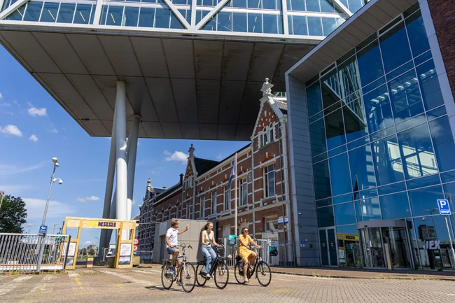 De Kaai in Rotterdam: moderne architectuur naast historische gebouwen met fietsers voor de ingang, onderdeel van gebiedsontwikkeling.