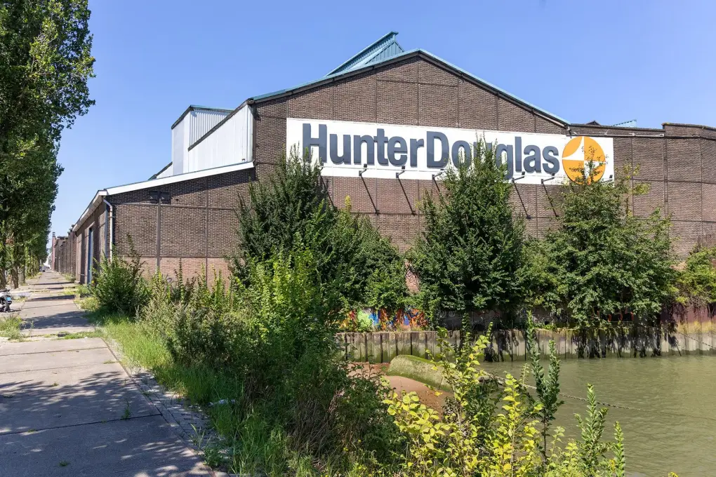 Foto toont de zijmuur van woningen met een groot bord van het bedrijf Hunter Douglas erop, gelegen aan het water.
