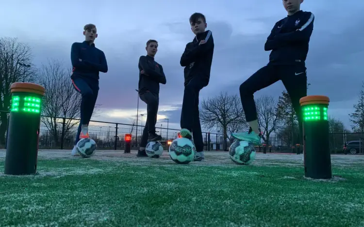 Vier mannen staan naast verlichte interactieve voetbalpalen op een kunstgrasveld.