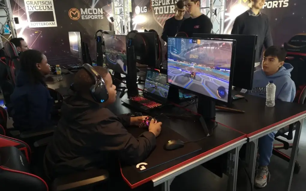 Een groep jongeren speelt een game achter computers in een esports-toernooiomgeving.