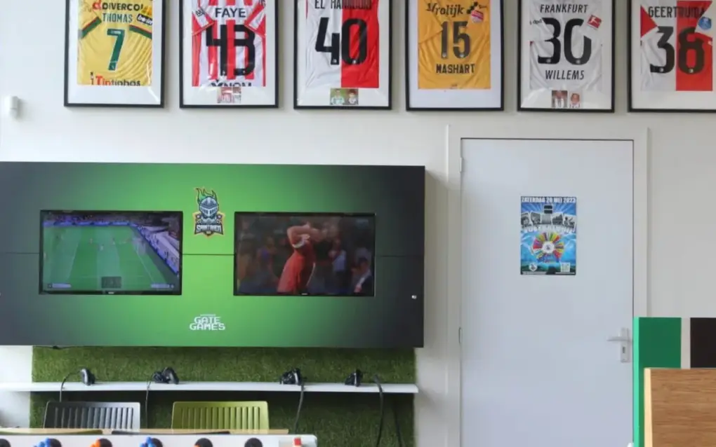 Een televisie toont een voetbalwedstrijd in een ruimte met sportshirts aan de muur.