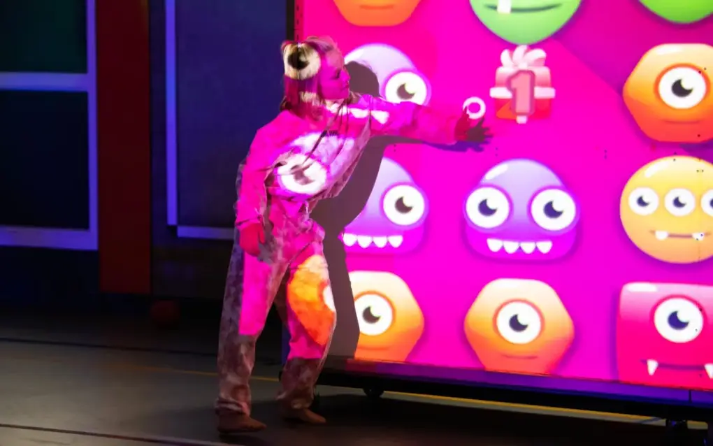 Een jongere werpt een bal tegen een verlichte interactieve muur met kleurrijke emoji-figuren.