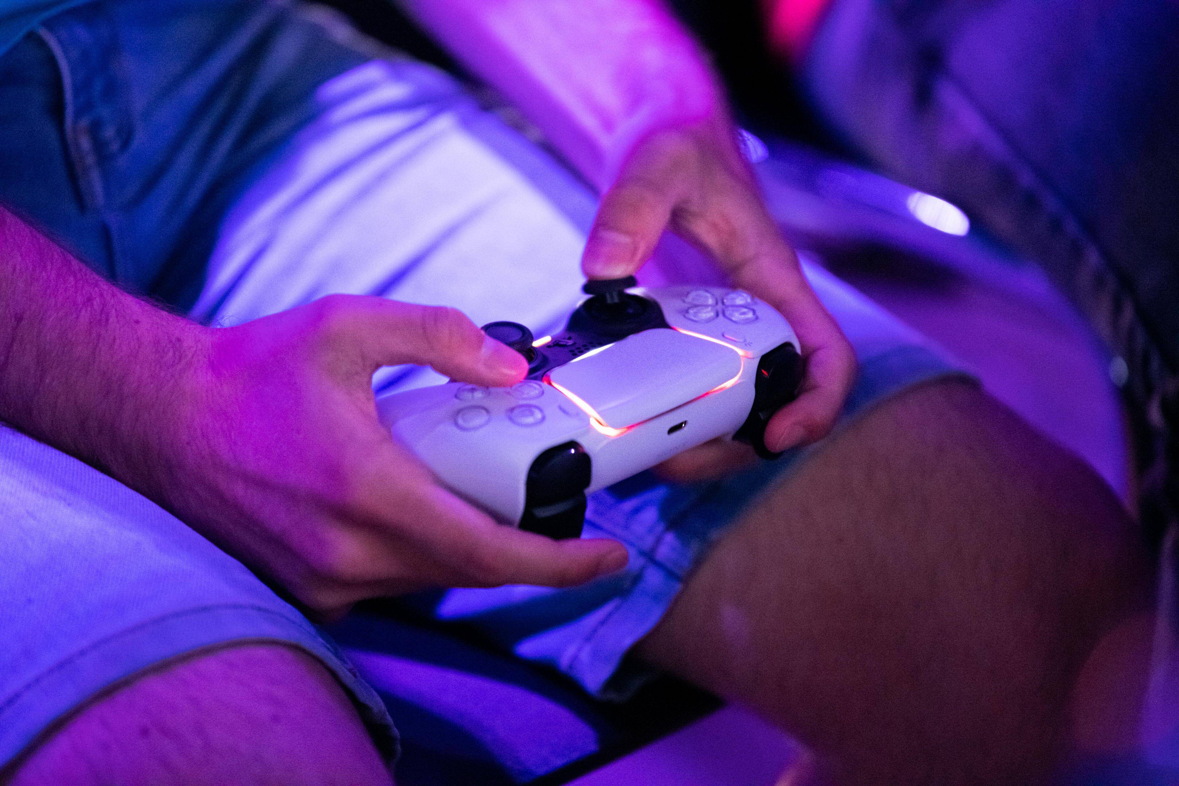 Close-up van iemand die een witte gamecontroller vasthoudt met paarse verlichting op de achtergrond.
