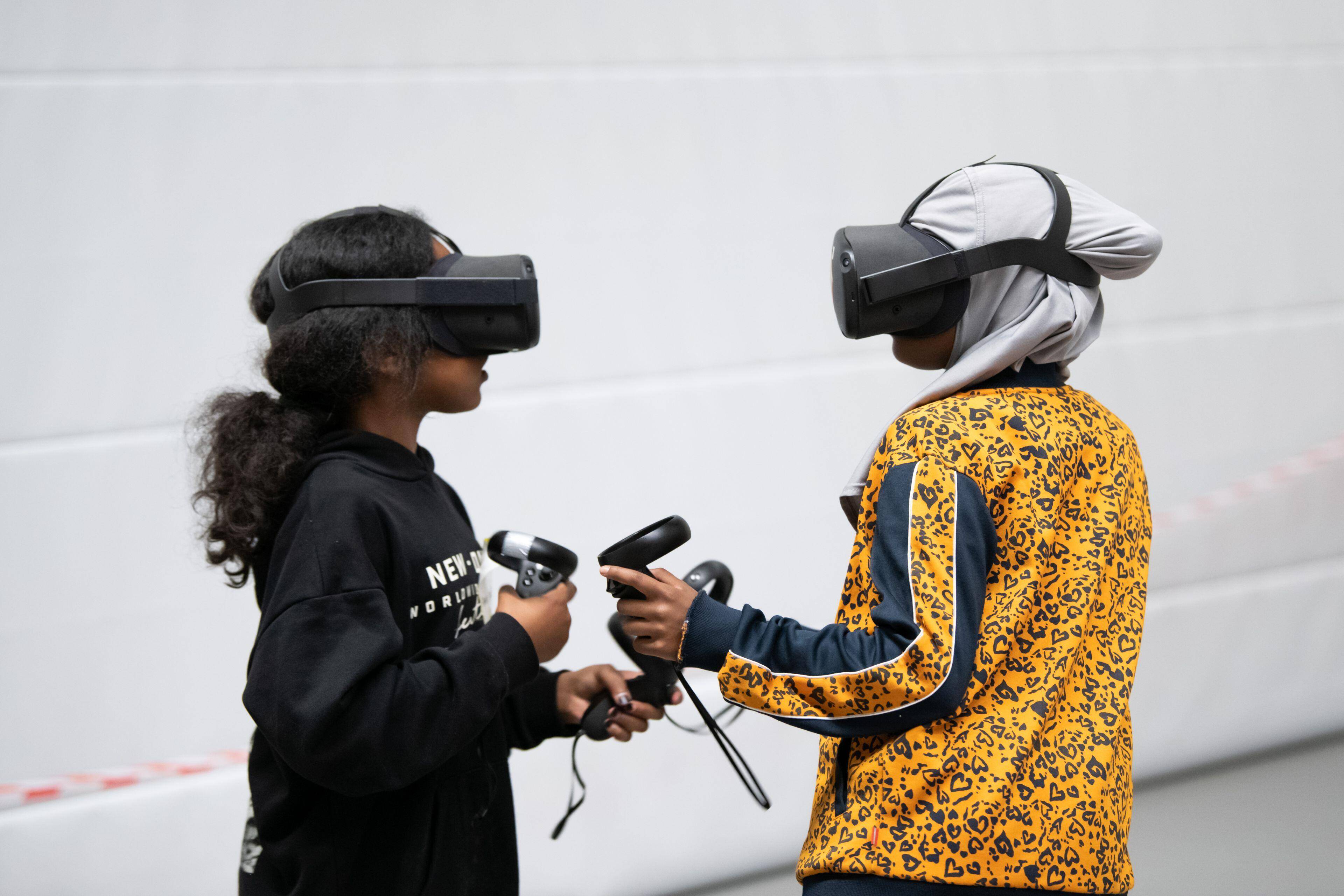 Twee meisjes dragen VR-brillen en houden controllers vast terwijl ze elkaar aankijken.