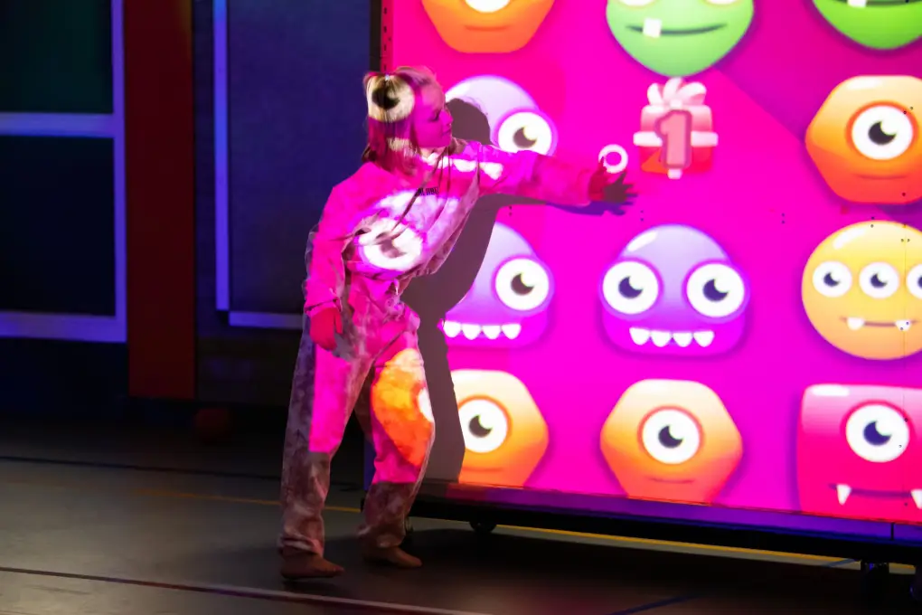 Een jongere in sportkleding raakt de interactieve muur aan waarop grote emoji-figuren en scores verschijnen.